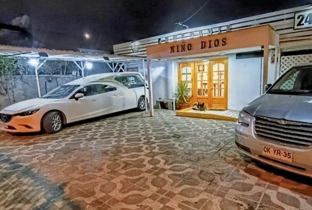 Fachada nocturna de Funeraria Niño Dios con vehículos funerarios